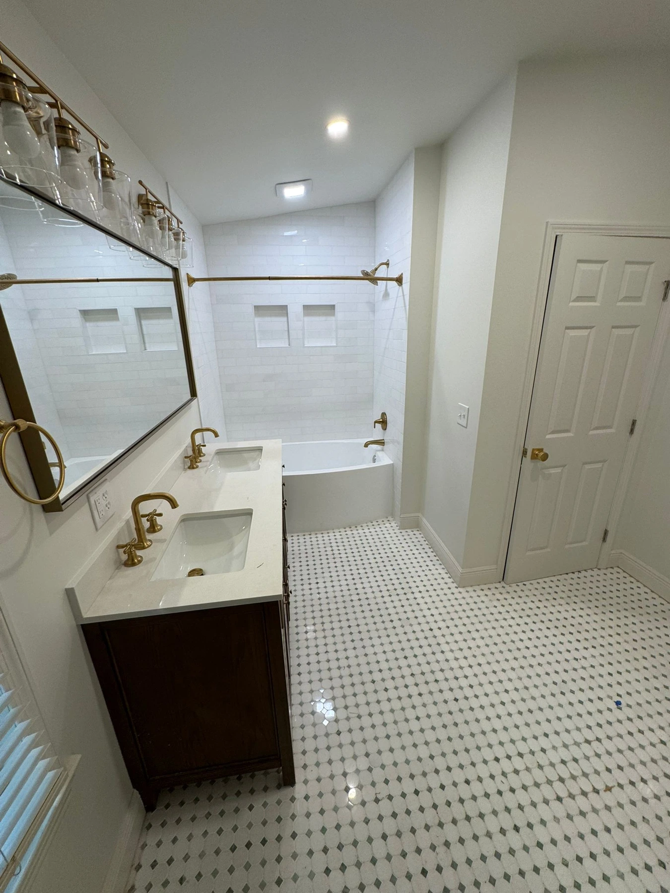 Finished bathroom with double vanity, brass fixtures, white tile and patterned mosaic floor