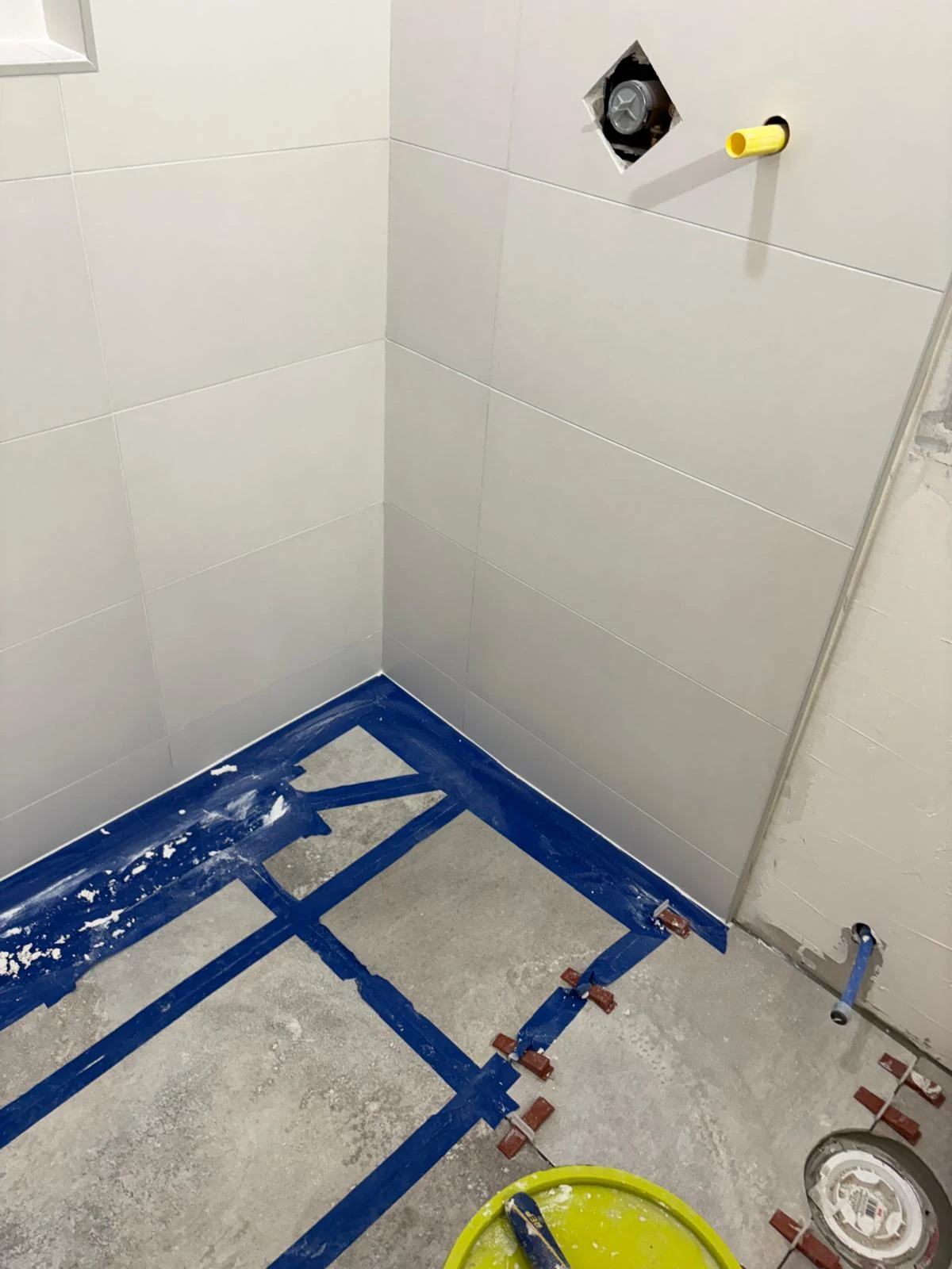 White tiled shower with protective tape and tools